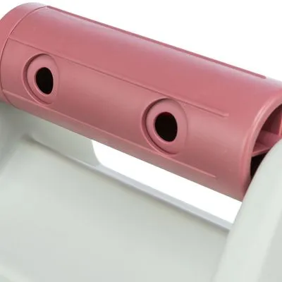 Detail van een roze kunststof handvat met drie ronde openingen, bevestigd aan een wit onderdeel. Materiaal: plastic.