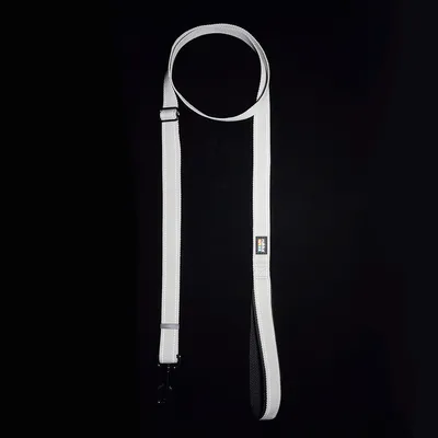 Bílé vodítko pro psy s černou rukojetí a kovovou karabinou, viditelné logo na vodítku.