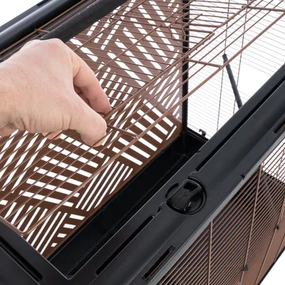 Hand öffnet braunes Metallgitter eines Käfigs mit schwarzem Rahmen, zeigt einfache Bedienung des Verschlussmechanismus.
