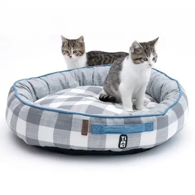 Grå, rutig kattsäng med blå kant och Tiaki-logo. Två kattungar sitter i den.