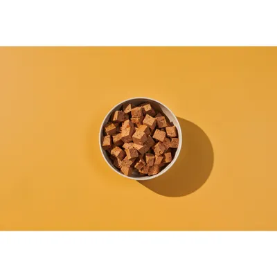 Bowl filled with small brown food cubes, shown on a plain yellow background.