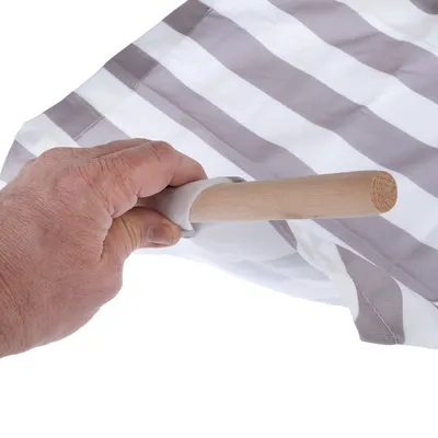 Hand leidt een houten stok door een stoffen lus met grijs-witte strepen. Demonstratie van de montage van een product.