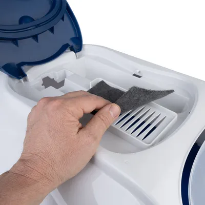 Hand zeigt, wie ein Filter in einen weissen Luftreiniger mit blauem Deckel eingesetzt wird.