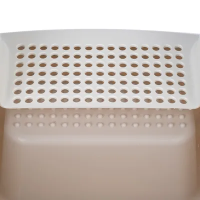 Primer plano de un arenero beige y blanco para gatos con estructura de tamiz para fácil limpieza.