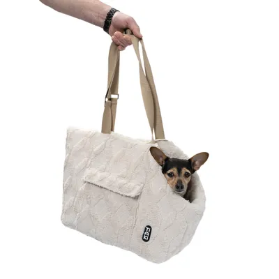Sac de transport en tissu beige avec anses, poche latérale et étiquette TIAKI, petit chien à l'intérieur, oreilles visibles par l'ouverture.