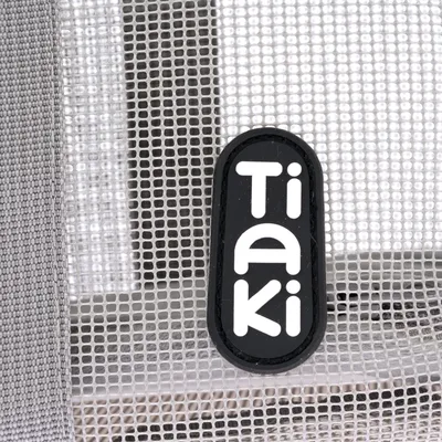 Inscription visible : Tiaki sur une étiquette noire, fixée à un tissu en maille grise et blanche.