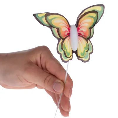 Hand hält einen bunten Schmetterling aus Papier mit weissem Körper an einem dünnen Stab.