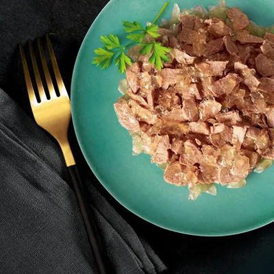 Nahaufnahme von zerkleinertem Fleisch in Gelee auf einem grünen Teller, garniert mit Petersilie. Goldene Gabel und schwarzes Tuch daneben.