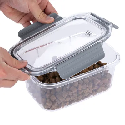Transparente opbergbox met grijze deksel, gevuld met droogvoer. Handen openen het deksel van de box.