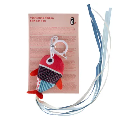 TIAKI Ring Ribbon Fish Juguete para gatos, pez de tela rojo con cuerpo estampado y cintas azules. Instrucciones visibles en fondo multilingüe.