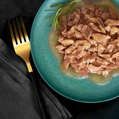 Chunks of meat in gravy served on a green plate with a sprig of rosemary, shown for product texture and appearance.