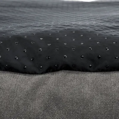 Nahaufnahme eines schwarzen, wasserabweisenden Materials mit Tropfenstruktur und grauem Stoff darunter.