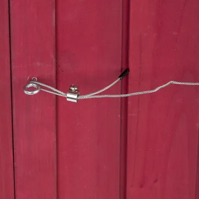 Detailaufnahme eines roten Holzpaneels mit einem silbernen Drahtseil, das durch eine Öse und einen Verschluss geführt ist.
