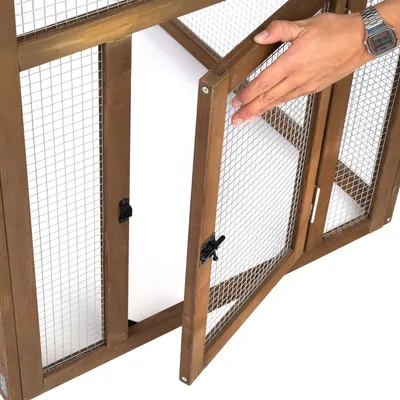Porte grillagée en bois avec loquet, ouverte par une main. Structure en métal et bois visible, adaptée pour enclos ou cage d’animaux.