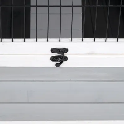 Detailansicht eines schwarzen Metallverschlusses an einer weissen Holztür mit grauer Verkleidung und Gitterelementen.