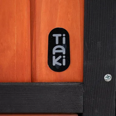 Tiaki logo na drevenom povrchu s čiernym rámom a viditeľnou skrutkou.
