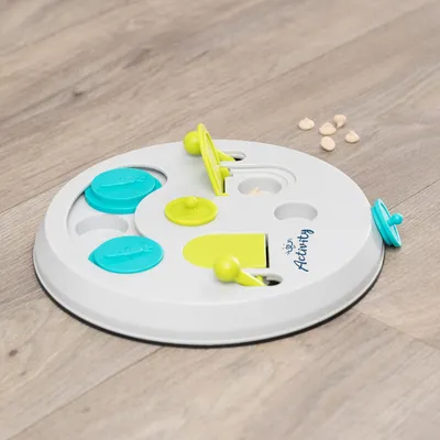 Rundes Intelligenzspielzeug mit gelben und blauen Elementen, Marke 'Activity', auf Holzboden. Sichtbare Leckerlis neben dem Spielzeug.