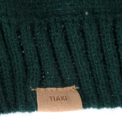 Nahaufnahme eines dunkelgrünen Strickmaterials mit braunem Lederetikett, auf dem 'TIAKI' steht.