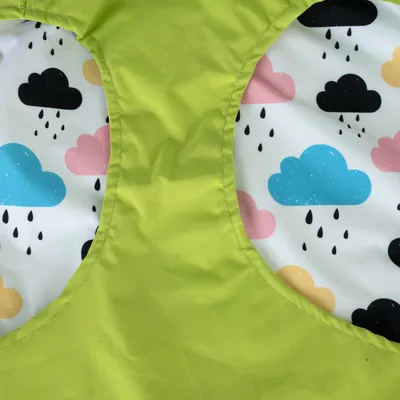 Détail d’un tissu imperméable vert avec doublure à motifs de nuages colorés et gouttes de pluie, visible sur un vêtement ou accessoire pour animal.