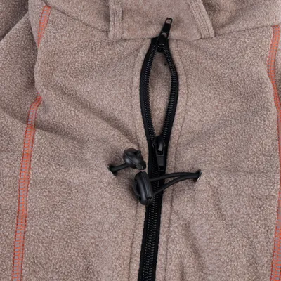Gros plan sur une fermeture éclair noire et un cordon de serrage avec stoppeurs sur tissu polaire beige, coutures orange visibles des deux côtés.