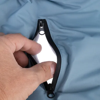 Gros plan sur une main ouvrant une poche zippée en tissu bleu, doublure blanche visible à l’intérieur. Fermeture éclair noire.