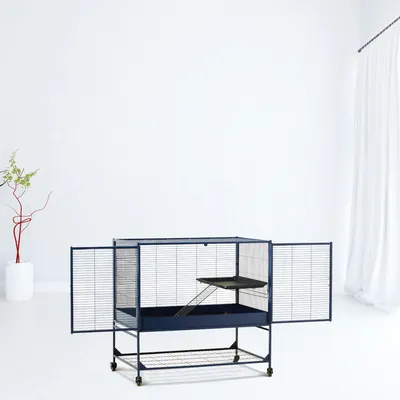 Grande cage métallique sur roulettes avec deux portes ouvertes, une rampe et une plateforme intérieure, fond bleu foncé, étagère inférieure visible.