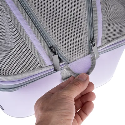 Gros plan sur une main tenant la poignée d’un sac de transport en tissu avec deux fermetures éclair visibles et parties en maille grise.
