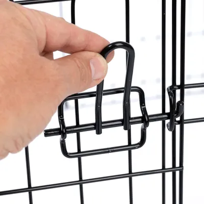 Hand zeigt, wie ein schwarzer Metallverschluss an einem Gitterkäfig geöffnet wird.