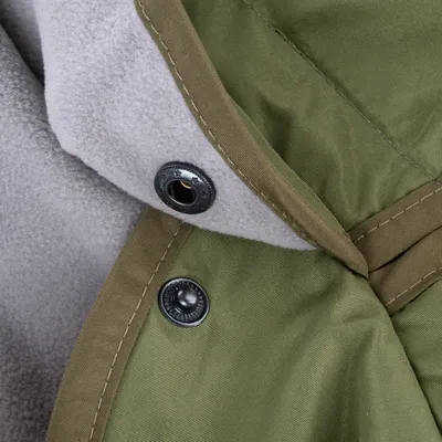 Gros plan sur un tissu vert avec doublure polaire grise et boutons-pression métalliques visibles, montrant les matériaux et la finition du produit.