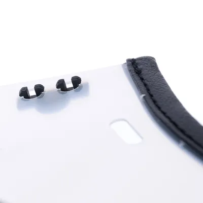 Gros plan sur une plaque blanche avec deux attaches noires en plastique et un bord recouvert de simili cuir noir, sans autres éléments visibles.