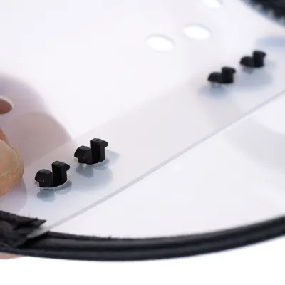 Gros plan sur une plaque transparente en plastique avec quatre attaches noires et des trous ronds visibles, bordure noire en tissu.