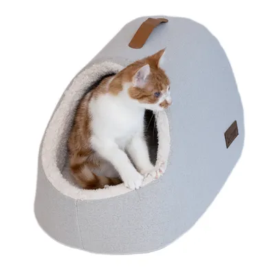 Kattenhuis van grijze stof met zachte, crèmekleurige rand. Rood-witte kater zit in de opening. Leren handvat bovenop en merklabel zichtbaar.