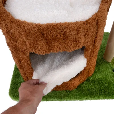 Una mano levanta un cojín blanco extraíble de una cueva marrón y mullida sobre fondo verde. Muestra la función del acolchado extraíble.