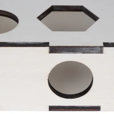 Boîte en bois clair avec ouvertures de formes différentes, dont un cercle et un hexagone visibles sur la surface.
