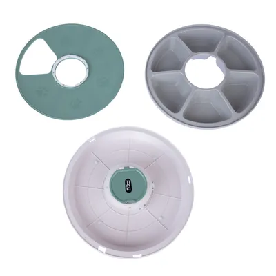 Three interchangeable inserts for the TIAKI food dispenser: green lid with paw pattern, grey insert with six compartments, and white container with green centre.