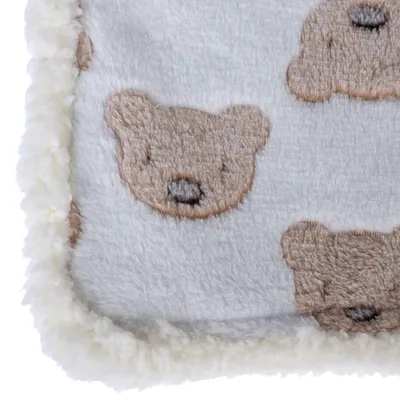 Närbild av en vit filt med bruna björnmotiv och fluffig kant.