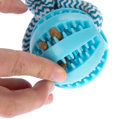 Juguete interactivo azul de plástico con pinchos, relleno de premios o pienso, sostenido por una mano. Tela azul y blanca visible en el fondo.