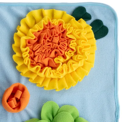 Snusetæppe af stof i blomsterform med gule, orange og grønne elementer på blå baggrund.