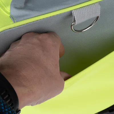 Hånd rækker ned i en gul taske med gråt inderfor og metalring. Detaljebillede af produktets funktionalitet.