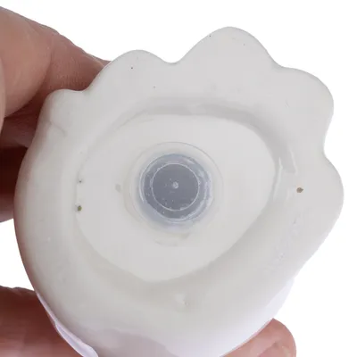 Vue rapprochée du dessous d’un objet en céramique blanche avec un bouchon rond en plastique transparent au centre, tenu par une main.