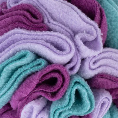 Nærbillede af stoflag i lilla, turkis og violet. Materialestruktur synlig.