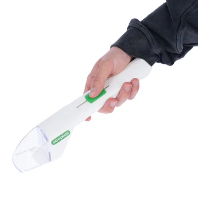 Kézben tartott fehér Zooplus etetőadagoló zöld csúszkával és átlátszó tartállyal.