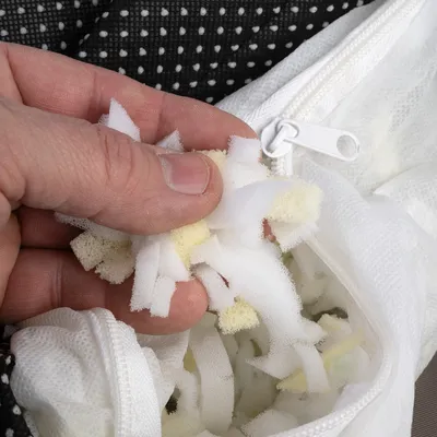 Kéz egy fehér, cipzáras tasakba nyúl, amely habszivacs töltettel van megtöltve.
