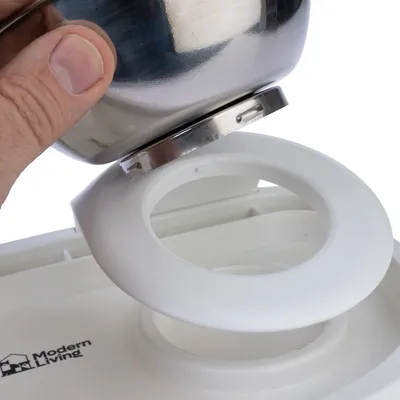 Hand showing how a stainless steel bowl is inserted into the white holder of a feeder. 'Modern Living' logo visible on the holder.