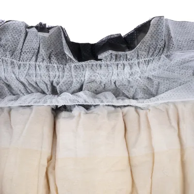Gros plan sur la texture et les couches d’un matériau absorbant en tissu non tissé, avec élastique visible. Couleurs : beige et gris.