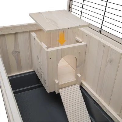 Intérieur d’une cage en bois pour rongeur avec maisonnette, rampe d’accès et toit amovible indiqué par une flèche jaune. Dessin de lapin gravé sur la maisonnette visible.