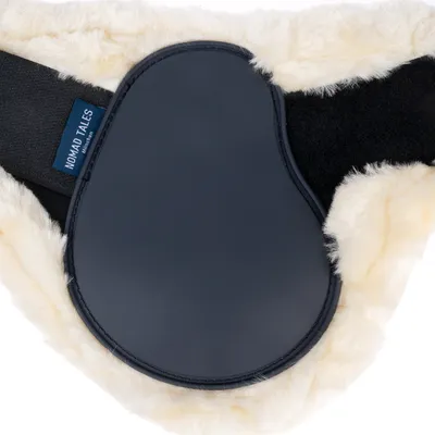 Détail d’un harnais avec doublure en fausse fourrure crème, plaque noire et étiquette bleue visible portant le nom de la marque Nomad Tales.