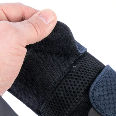 Gros plan sur une main ouvrant une fermeture auto-agrippante noire sur un accessoire en tissu avec étiquette taille L visible, surface en maille et renforts bleus à motif hexagonal.