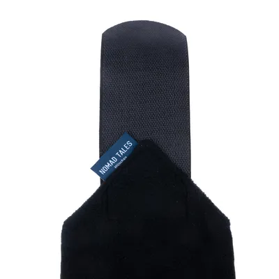Étiquette bleue avec texte visible : NOMAD TALES, Wanderer, fixée sur un tissu noir. Partie supérieure en matériau textile foncé.