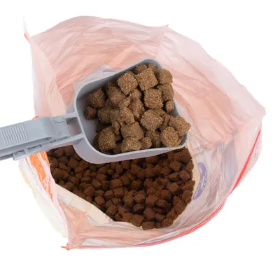 Felnyitott tasak barna száraztáppal, szürke kanál teli táppal a tasak felett.